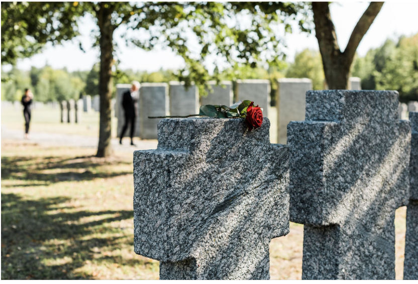 A red rose resting on a granite cross gravestone with mourners in the background