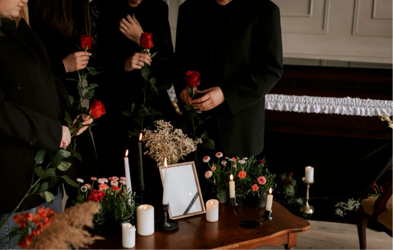 Family members in black holding red roses beside a memorial table with candles and flowers